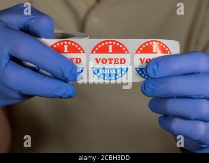 Hands in medical gloves holding roll of I Voted Today buttons ready for in person voters in Presidential election Stock Photo