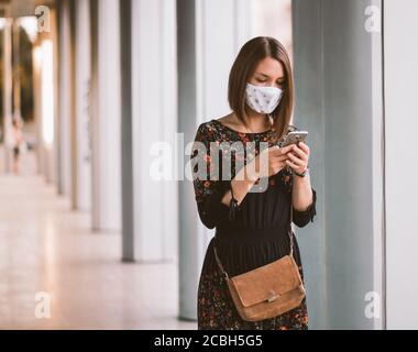 Young woman using smart phone in the city wearing face mask protection for virus coronavirus covid 19 Stock Photo