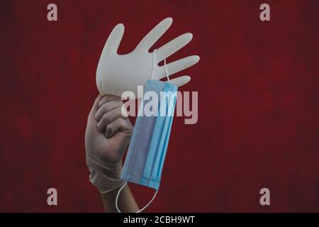 Medical mask hanging on inflated glove. hand holds white surgical glove with protective mask. red background Stock Photo