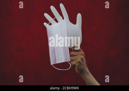 Medical mask hanging on inflated glove. hand holds white surgical glove with protective mask. red background Stock Photo