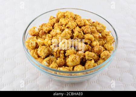 Caramel popcorn in glass snack bowl on white textured tablecloth Stock Photo