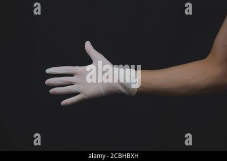 Hand in medical glove reach out. gesturing hand in white protective glove on a black background Stock Photo