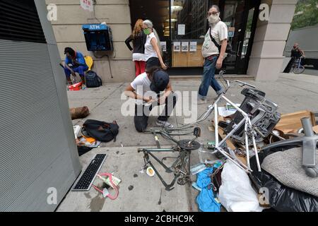 New York City, USA. 13th Aug, 2020. A man who identified himself only as John, works on dismantling a bicycle to sell for parts along 6th Avenue near 24th Street, part of an encampment set up by homeless persons, in the Chelsea neighborhood of Manhattan, New York, NY, August 13, 2020. Despite a visit by New York City Mayor Bill de Blasio who asserted that the issue of homelessness will be addressed, but local residents and business owners are upset over sanitary and safety issues. (Anthony Behar/Sipa USA) Credit: Sipa USA/Alamy Live News Stock Photo