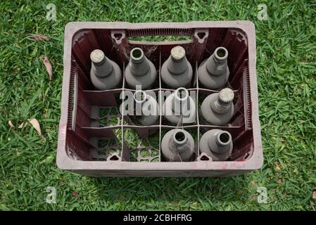 Top view of an old red plastic box full of covered in dust empty bottles of beers laying outside in the garden. Stock Photo