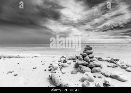 Stacked stones over the sea at sunset. Balanced stones stacked to a tower on the beach, clouds with dramatic sky Stock Photo