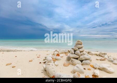 Stacked stones over the sea at sunset. Balanced stones stacked to a tower on the beach, clouds with dramatic sky Stock Photo