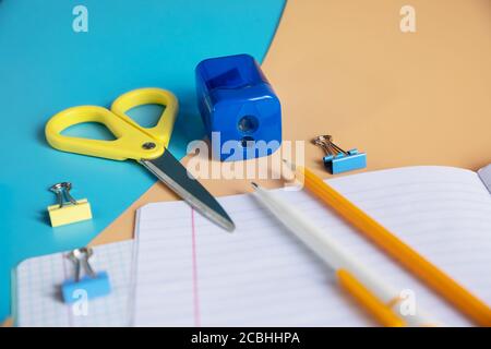 Concept back to school. School stationery. notepad with blank page, pens, pencils, sharpener, paper clips on orange and blue background.Arrangement of Stock Photo