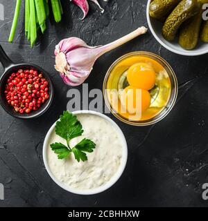 Homemade white sauce tartar tartare with ingredients pickles, capers, dill, parsley, garlic, lemon on black stone table top view square Stock Photo
