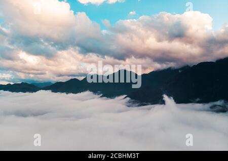 Background photo of low clouds in a mountain valley, vibrant blue and orange sky. Sunrise or sunset view of mountains and peaks peaking through clouds Stock Photo