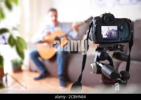 Camera recording video blogger doing a review of a guitar in the living room Stock Photo