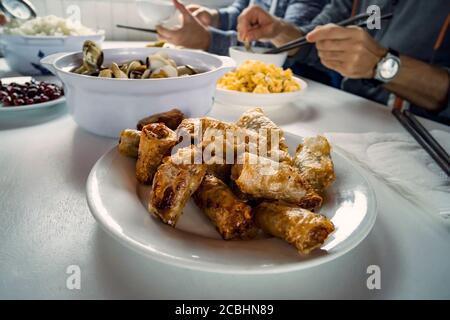 Fried spring rolls on a white plate on a table in a restaurant, in front of people. Stock Photo