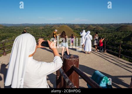 Bohol / Philippines - July 18, 2019: Christian Catholic nun taking photo with smartphone in the famous Chocolate Hills of Bohol Stock Photo