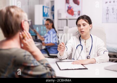 Senior woman having problem with sore neck. Young doctor wearing white coat and stethoscope during examination of old patient. Stock Photo
