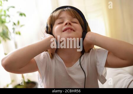 Little girl listening passionately to music holding earphones in a warm room at home Stock Photo