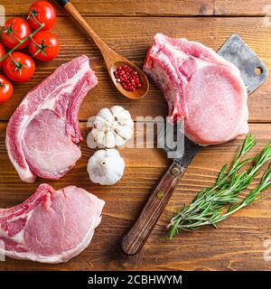 Raw pork meat chopes with herbs and spices with meat american cleaver on wooden background side view space for text. Square Stock Photo