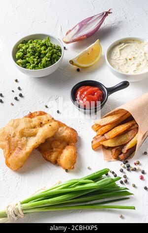 Fish & chips with dip and lemon in a paper cone on white background with all components classic recipe takeaway food white stone textured background Stock Photo