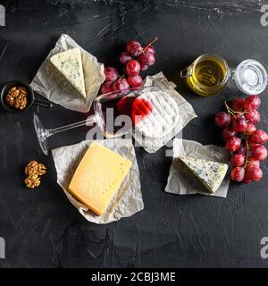 Grapes, red wine, cheeses, brie cheese , blue, chease honey and nuts over black background top view square Stock Photo