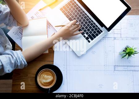 architect , engineering , creative and designer workspace concept : Top view of Asian female architect working with blueprint , notebook and laptop Stock Photo