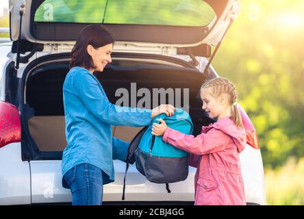 Mother giving backpack to daughter from car trunk before school Stock Photo