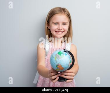 Schoolgirl holding small globe in front of her on gray background Stock Photo