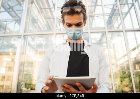 Young male plant researcher wearing mask while using digital tablet at greenhouse Stock Photo