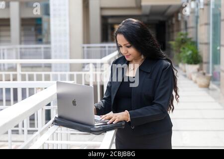 An Indian woman works on her laptop in an urban corporate setting, Stock Photo