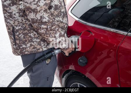 Man holding fuel pump nozzle with filling benzine oil in red car on winter in self-service petrol station Stock Photo
