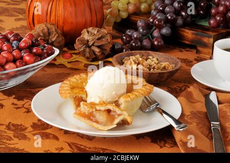 An individual serving of apple pie with ice cream on a holiday table