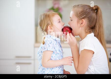 Two children eat a red apple together in the kitchen Stock Photo