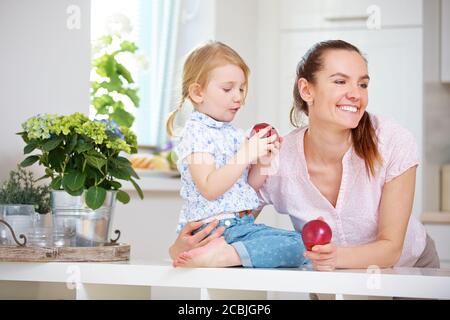 Family with mother and daughter eating apple in the kitchen Stock Photo
