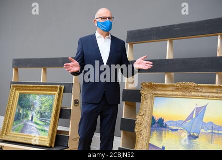 14 August 2020, Brandenburg, Potsdam: Dietmar Woidke (SPD), Prime Minister of Brandenburg, stands during his press tour with blue mouth-nose protection in the Barberini Museum between the paintings 'Allee de la Villa des Fleurs a Trouville' (l, 1883) by Gustave Caillebotte, and 'The Harbor at Sunset, Opus 236 (Saint-Tropez 1892)' by Paul Signac. During the closing phase of the house, there was a view of the new exhibition 'Impressionism. The Hasso Plattner Collection', which will open on 07.09.2020. Potsdam is thus to become one of the most important centres of collections of Impressionist lan Stock Photo