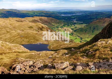 Sticlke Tarn seen from Pavey Ark fell in the Langdales with the Langdale valley green fields and Lake Windermere in the distance.