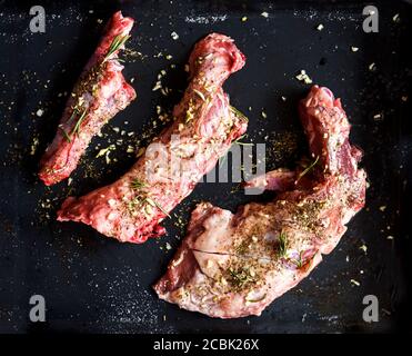 Lamb meat bbq preparation. Lamb chops with spices and rosemary on black rustic plate from above. Top view of restaurant cuisine barbecue. Stock Photo