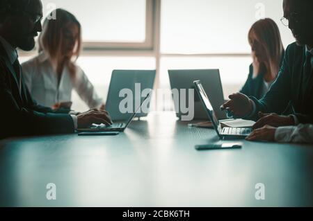 Silhouettes of business people working together on computers while sitting symmetrically at office table against background of sunlit window. Business Stock Photo