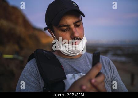 A shallow focus of a young male with a facemask taking a picture with his phone at Chiclana beach, Spain Stock Photo