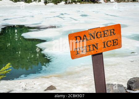 Thin ice warning notice on orange danger signboard by mountain lake Stock Photo