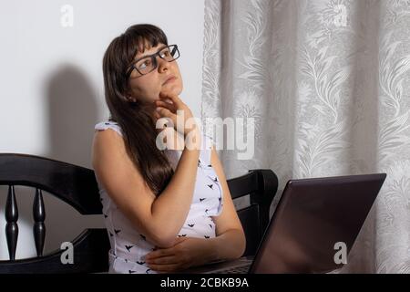 A girl with glasses works sitting at a laptop on a bed. Work from home, distance learning. Stock Photo