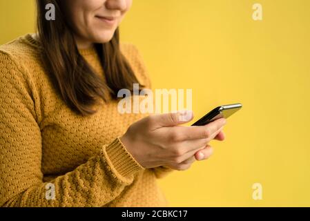 Woman in yellow sweater smiling and using smartphone Stock Photo