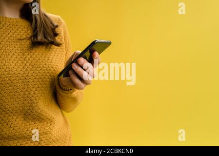 Woman in yellow sweater using smartphone. Holding Stock Photo