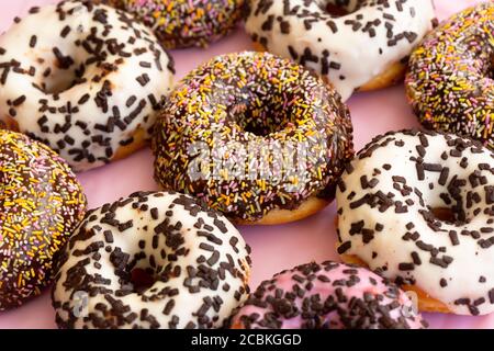Close up view of delicious colourful donuts with sprinkles and chocolate flakes . Assorted donuts with chocolate frosted, white and pink glaze and sprinkles. Selective focus. Stock Photo