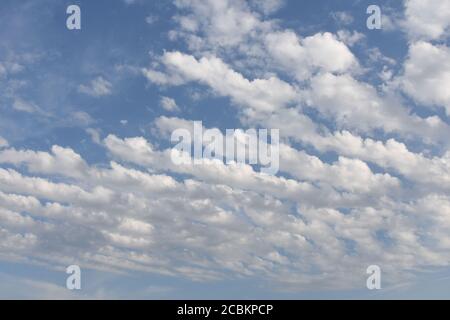 Azure blue sky with white cirrocumulus and alto cumulus woolpacks or heap clouds during sunny summer day over Swiss countryside. Stock Photo