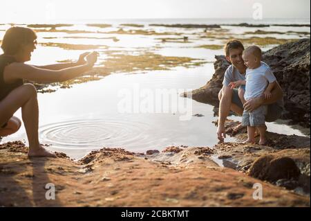 Mother taking photograph of father and son, on beach Stock Photo