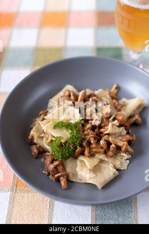 Pappardelle pasta with wild foraged chanterelle mushrooms in a creamy white wine sauce in a grey bowl on a table cloth Stock Photo