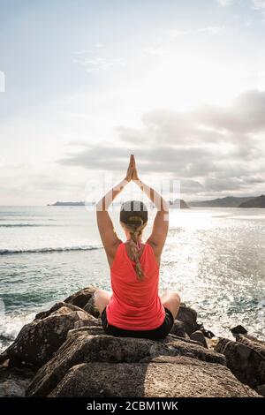 Tourist practising yoga on rocks, Mawi Beach, Lombok, Indonesia Stock Photo