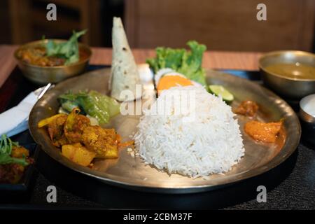 Indian metal plate with rice, chicken and pita bread served with different sauces in a restaurant Stock Photo