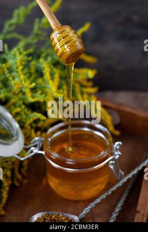 Honey in a glass jar with a wooden spoon. Still life on a wooden table with yellow flowers Goldenrod. Healthy sweet food. Close up with selective Stock Photo