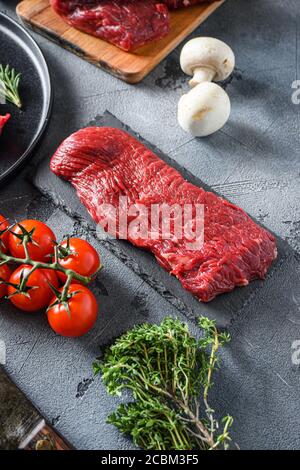 Raw tri tip, bottom sirloin cut steak on black slate raw organic food , marbled beef over other alternative cuts with herbs tomatoes peppercorns over Stock Photo