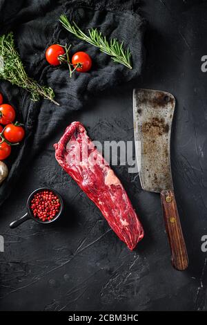 Organic machete or hanger butcher steak, near butcher knife with pink pepper and rosemary. Black background. Top view. Vertical Stock Photo
