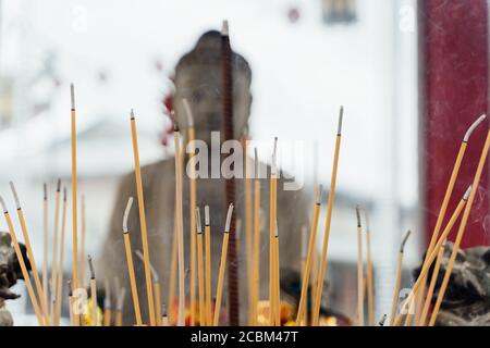 Selective focus on burning incense sticks in front of a Buddhist statue out of focus on the background Stock Photo