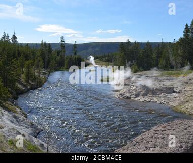 Late Spring in Yellowstone National Park: Mortar Geyser and Fan Geyser of the Morning Glory Group on the Bank of Firehole River in Upper Geyser Basin Stock Photo